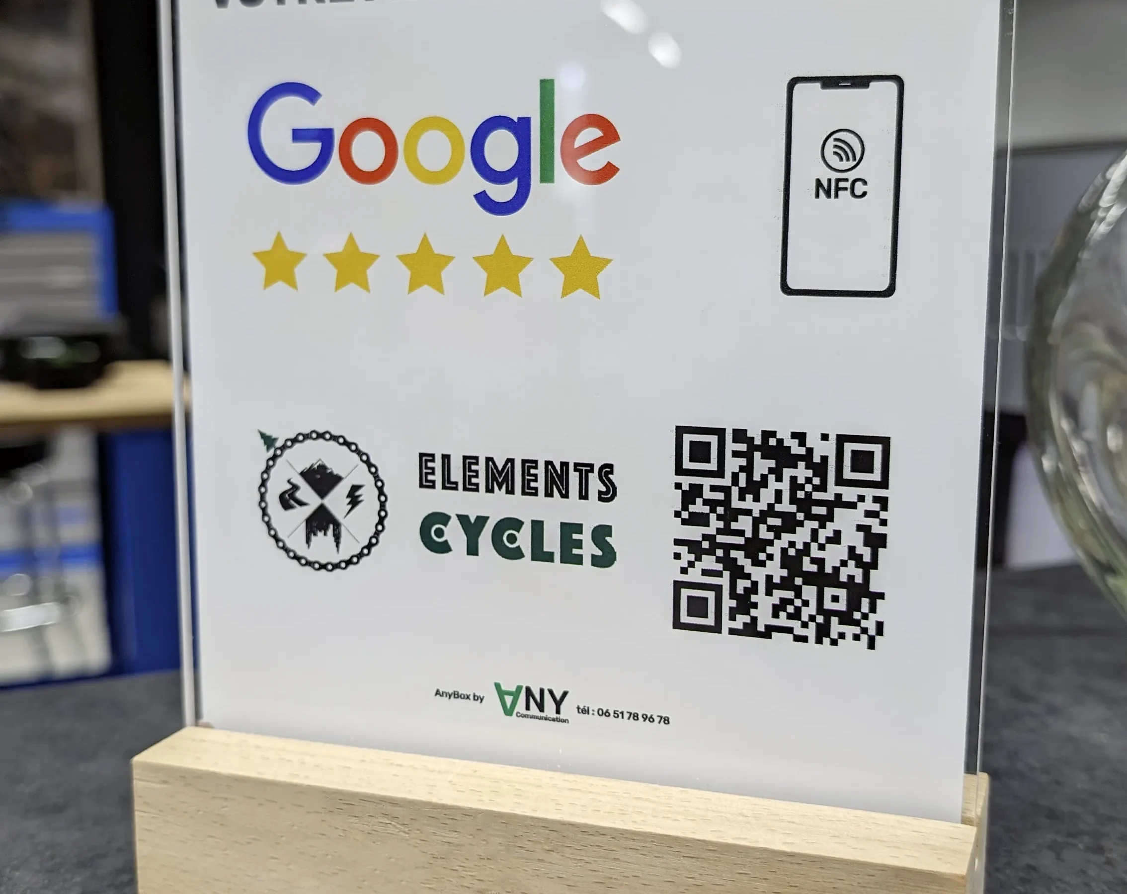 Photo d'un Récupérateur d'avis client AnyBox avec QR code et NFC sur support bois, pour Elements Cycles un magasin de vélos, posé sur un comptoir effet béton.